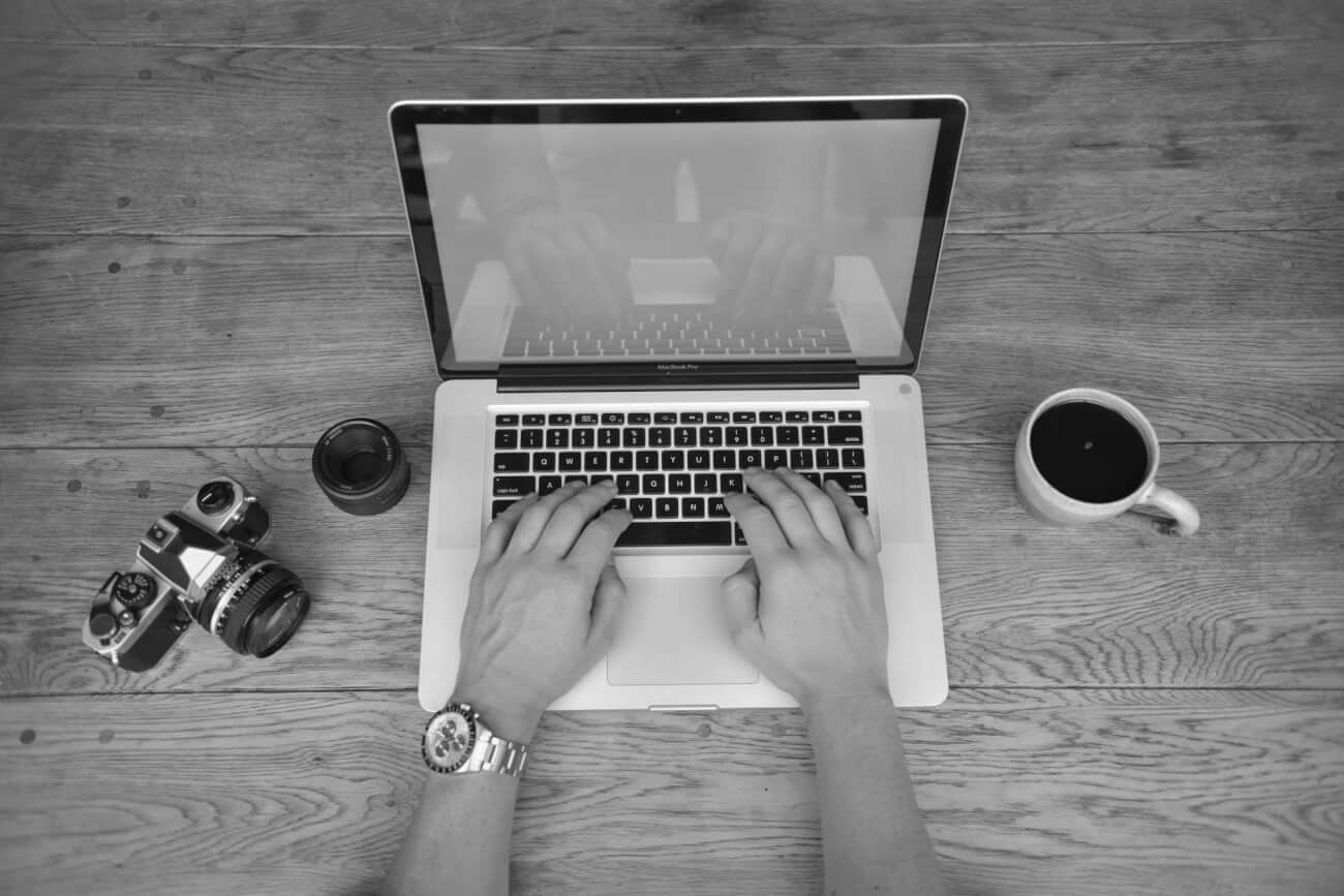 Hombre escribiendo en el ordenador portátil con la cámara retro y café