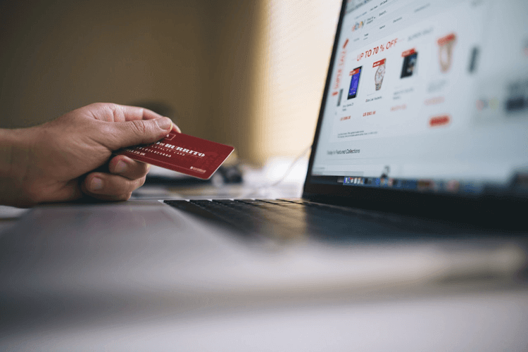 a person in front of a laptop holding a credit card