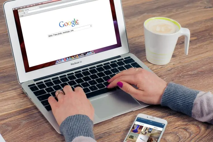 a women sitting in front of a computer with a coffee cup on the side and Google main page open
