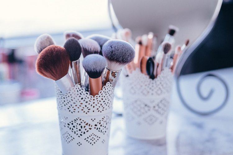 makeup brushes in white containers on a marble table, mirror in the background