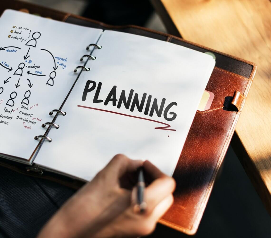 a person writing the word planning in block letters with a black pen in a notebook